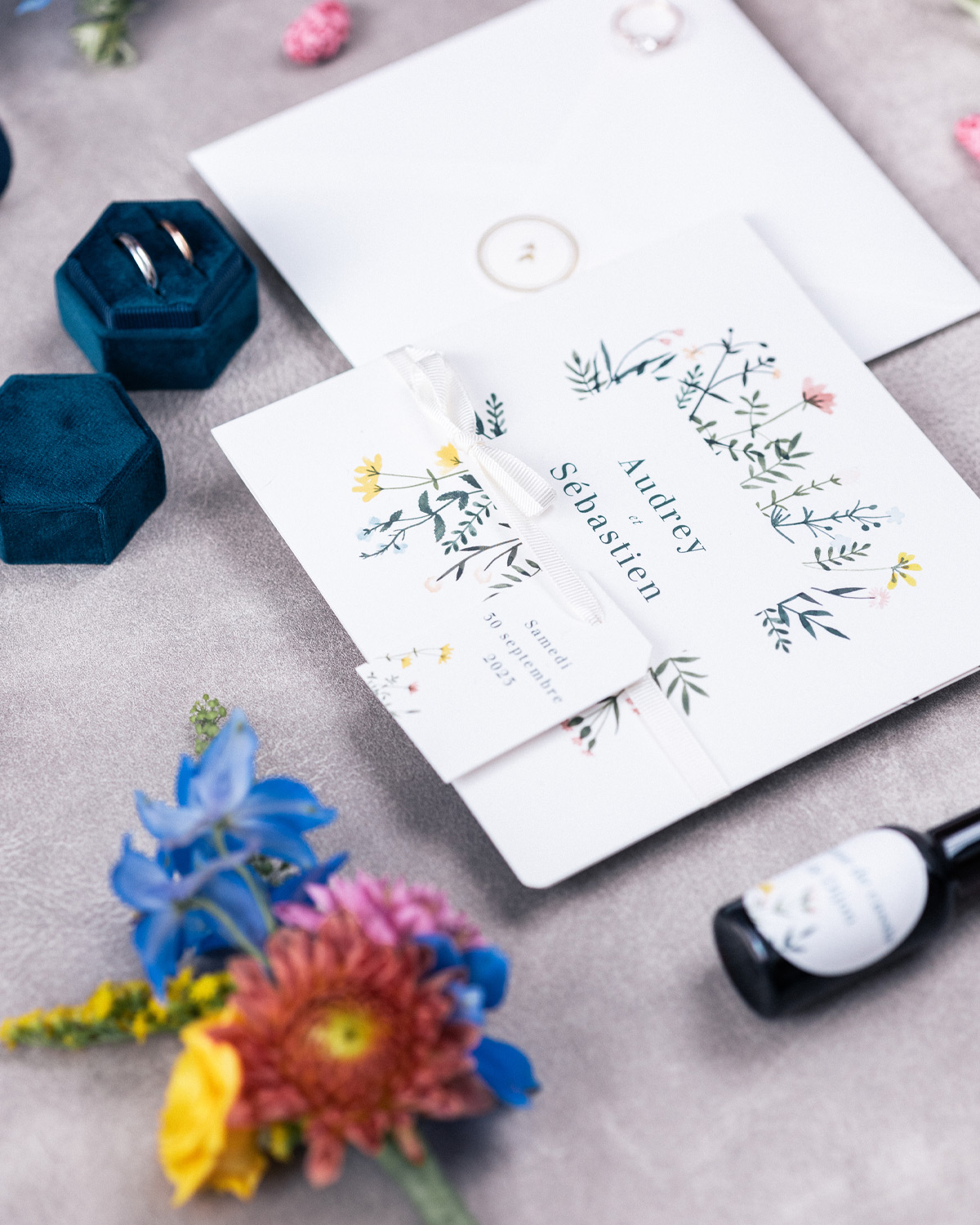 Faire-part de mariage personnalisé entouré de fleurs colorées avec alliances et accessoires de cérémonie